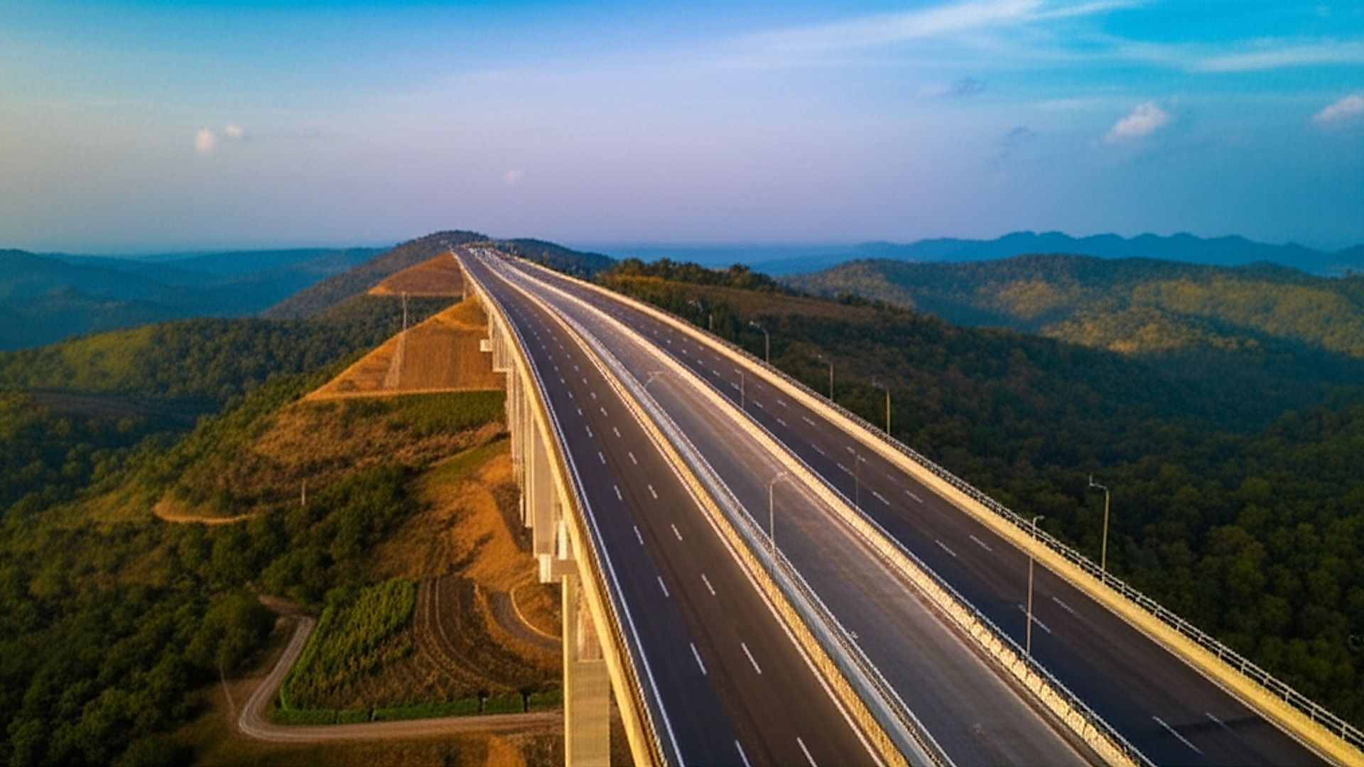High-angle architectural photograph showcasing a newly constructed four-lane expressway bridge spanning a lush, green valley in the Chakradharpur region of Jharkhand, India. Golden hour lighting, late afternoon, casts warm shadows highlighting the bridge's concrete and steel structure. Composition emphasizes the smooth asphalt roadway and meticulously landscaped embankments blending with the natural terrain. Clear blue sky with subtle cloud formations. Professional photography, sharp focus, realistic details, capturing the scale and integration of the infrastructure within the landscape. Show signage indicating the expressway route.. Professional architectural photography, ultra-high quality, sharp focus, vivid colors, dramatic lighting, golden hour, cinematic composition, 8K UHD, photorealistic.
