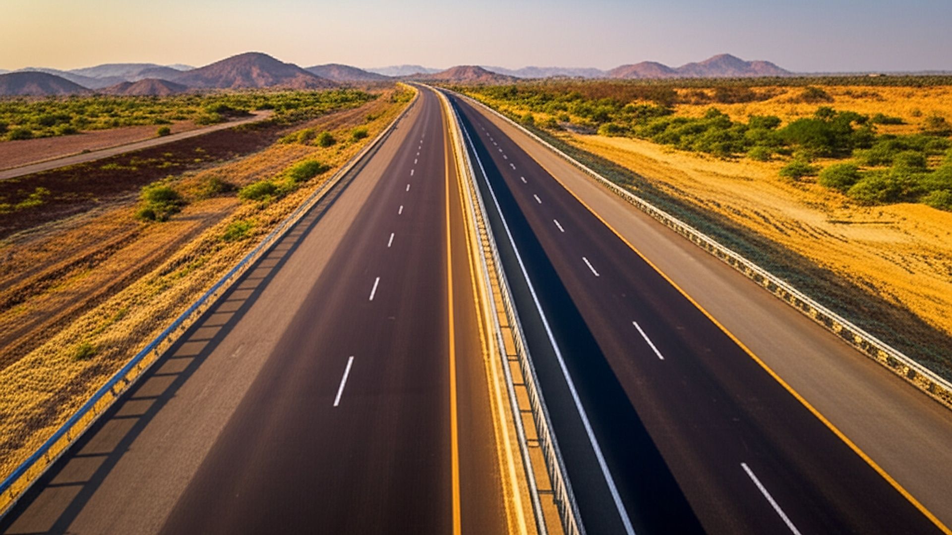 Architectural photograph showcasing the completed NH-754K 6-lane expressway near Deogarh, Rajasthan, India. Capture a sweeping vista of the highway, emphasizing its smooth asphalt surface and clear lane markings. Frame the image to include the surrounding arid Rajasthani landscape: sparse vegetation, distant hills, and the vast sky. Shoot during the golden hour – late afternoon – with warm, directional sunlight casting long shadows and highlighting the texture of the road and landscape. Professional architectural photography style, high resolution, focus on detail and showcasing the scale of the infrastructure.. Professional architectural photography, ultra-high quality, sharp focus, vivid colors, dramatic lighting, golden hour, cinematic composition, 8K UHD, photorealistic.